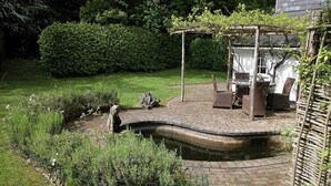 En have med et bassin, en pergola og udendørs møbler.