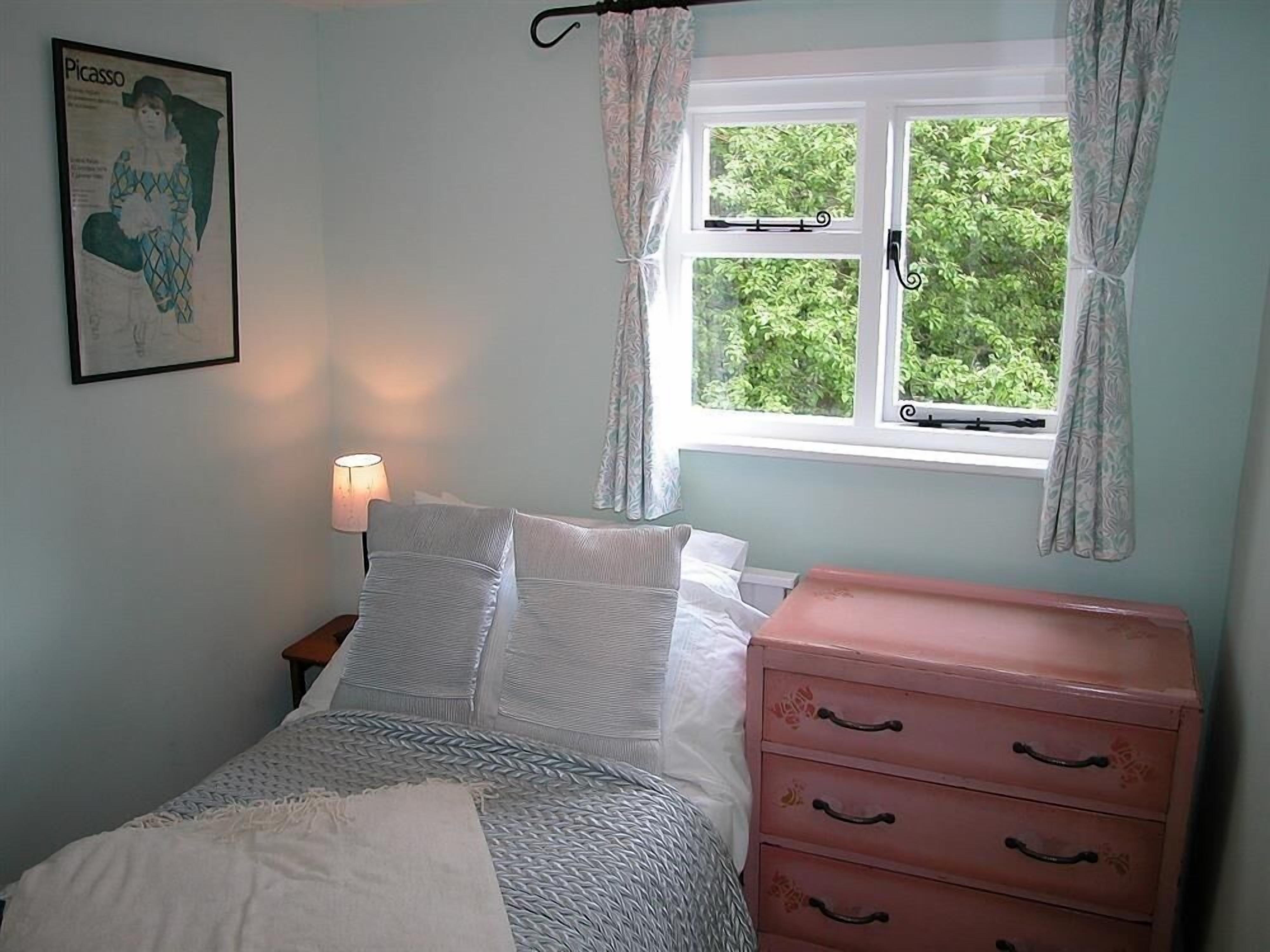 A bedroom with a bed, a nightstand, a dresser, a window with curtains, and a framed picture on the wall.