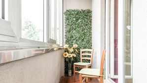 A narrow balcony with a concrete wall, a wooden chair, and a potted plant with sunflowers. - JOIVY Milano Fiera Cozy & Elegant Apartment (Milan)
