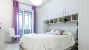 A modern bedroom with a bed, white wardrobe, and a chair. - JOIVY Milano Fiera Cozy & Elegant Apartment (Milan)