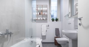 A modern bathroom with a glass-enclosed shower, a white sink, and a toilet. There is a shelf with decorative items above the sink.
