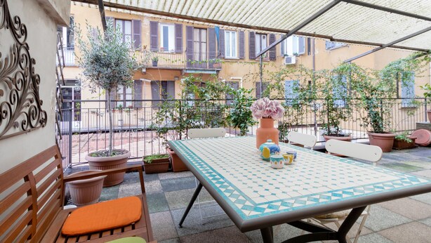 An outdoor patio with a table and chairs, surrounded by potted plants and a view of the neighborhood.