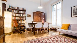 A cozy living room with a wooden cabinet, a dining table with chairs, a sofa, and a large bookshelf.