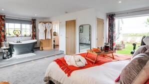 Ein modernes Schlafzimmer mit einem großen Bett, einer Badewanne und Blick auf den Garten.