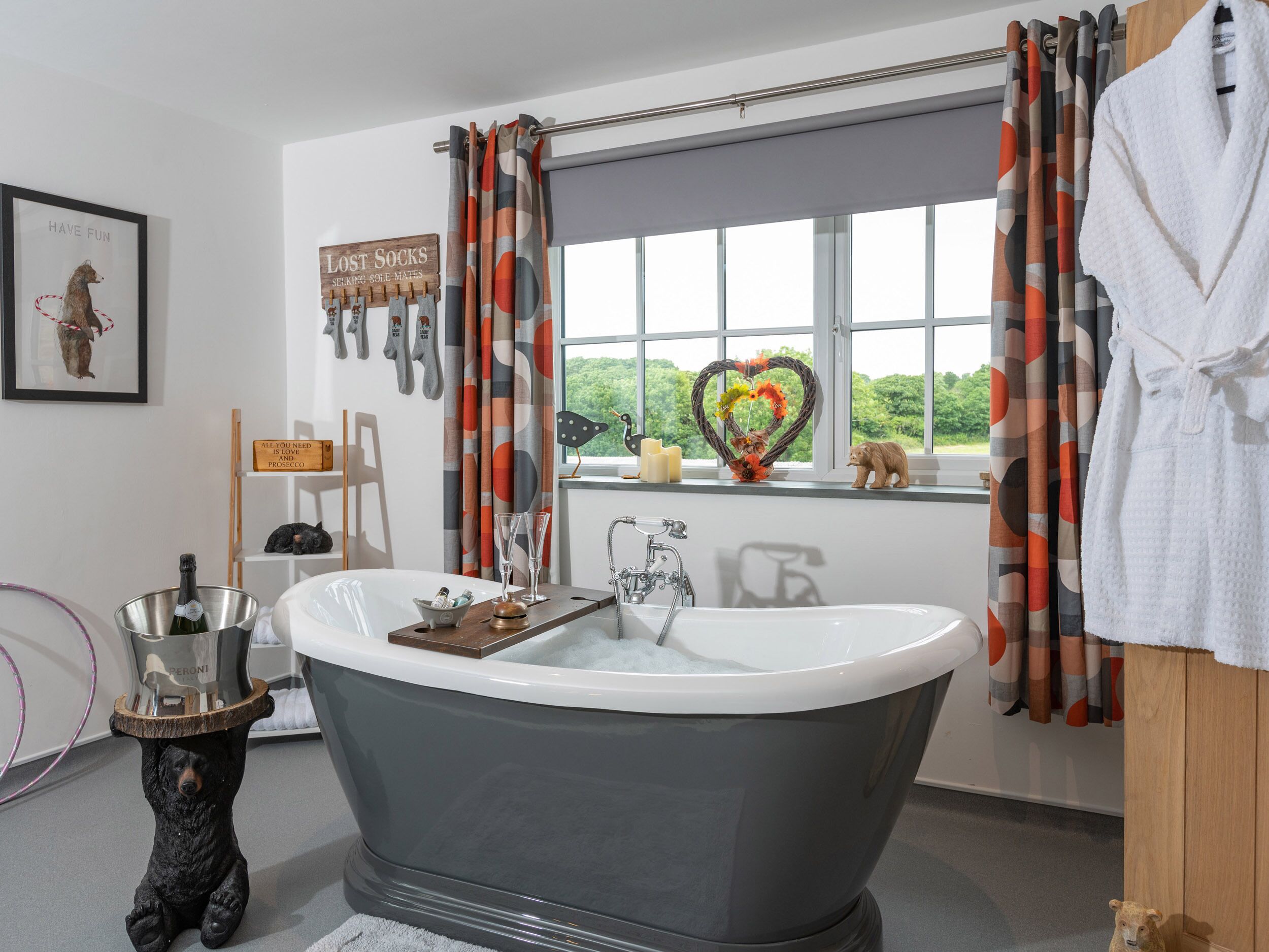 A bathroom with a freestanding bathtub, a window with a view of greenery, and a bear-themed decor.