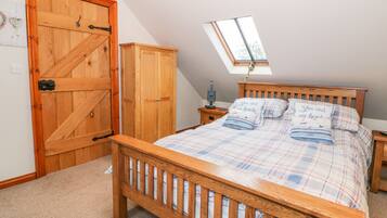 A bedroom with a wooden bed, a skylight, a wardrobe, and a nightstand.