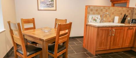 A dining area with a wooden table and chairs, a kitchen with a tiled backsplash, and a framed picture on the wall.