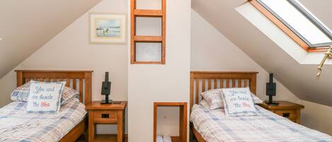 A bedroom with two beds, a skylight, a framed picture, and a bedside table with a lamp.