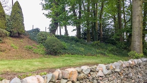 A stone wall with a grassy area and trees in the background. - Garden Cottage (Castle Douglas)