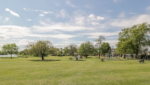 A park with a playground, picnic tables, and a lake in the background. - Garden Cottage (Castle Douglas)