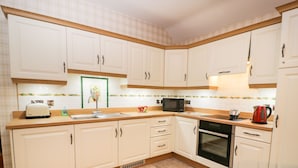 A kitchen with white cabinets, a microwave, a toaster, and a kettle. - Garden Cottage (Castle Douglas)