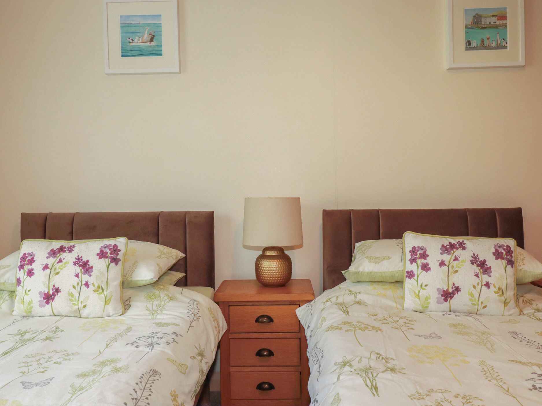 A double bed with floral bedding, a wooden nightstand with a lamp, and two framed pictures on the wall.