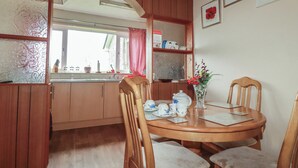 A wooden dining area with a round table, chairs, a vase with flowers, and a window with a view. - Underlanes (Camelford)