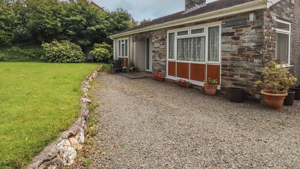 A stone house with a gravel driveway, a small garden, and a window with the text 'UNDERLANES'. - Underlanes (Camelford)