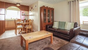 A living room with a brown leather sofa, a wooden coffee table, a dining area with a wooden table and chairs, and a cabinet with glass doors. - Underlanes (Camelford)