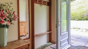 A room with a wooden dresser, a mirror, a wall-mounted coat rack, and a door leading to an outdoor area. - Underlanes (Camelford)