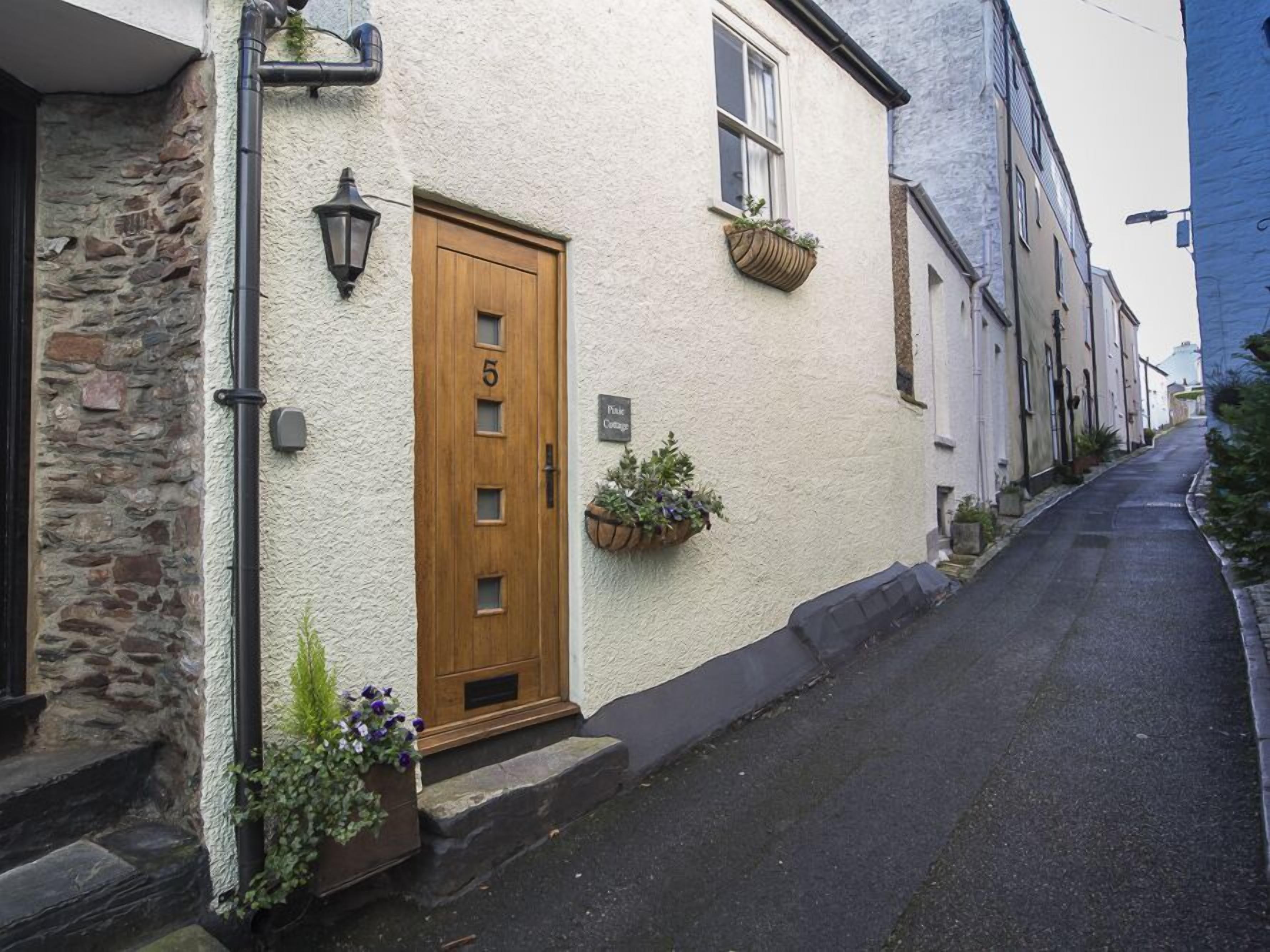 A narrow street with a building featuring a wooden door marked with the number 5, stone walls, and flower boxes on the windowsills.