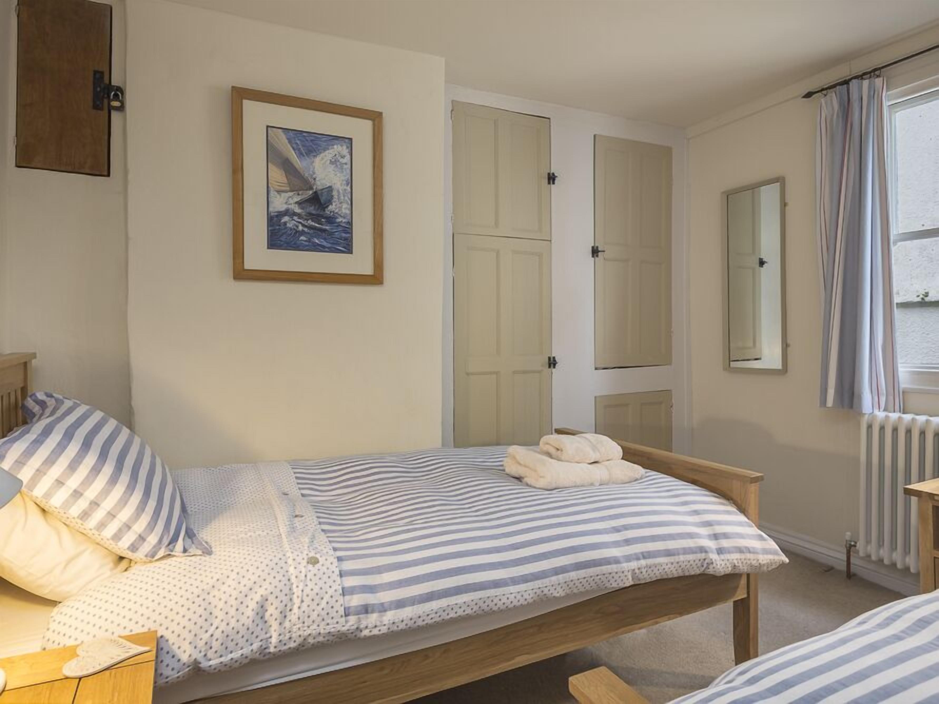 Une chambre avec un lit simple, une tête de lit en bois, un tableau encadré représentant un voilier, une fenêtre avec des rideaux et un radiateur.