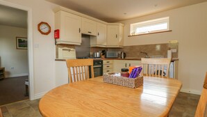 A compact kitchen with white cabinets, a wooden dining table, and a window above the sink.
