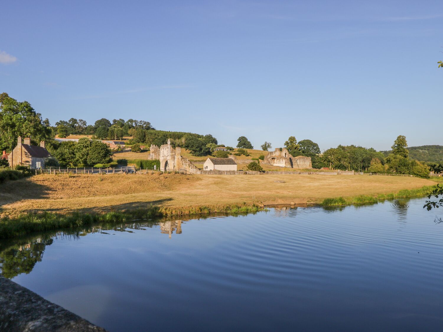 A historic site with ruins, a pond, and surrounding greenery.