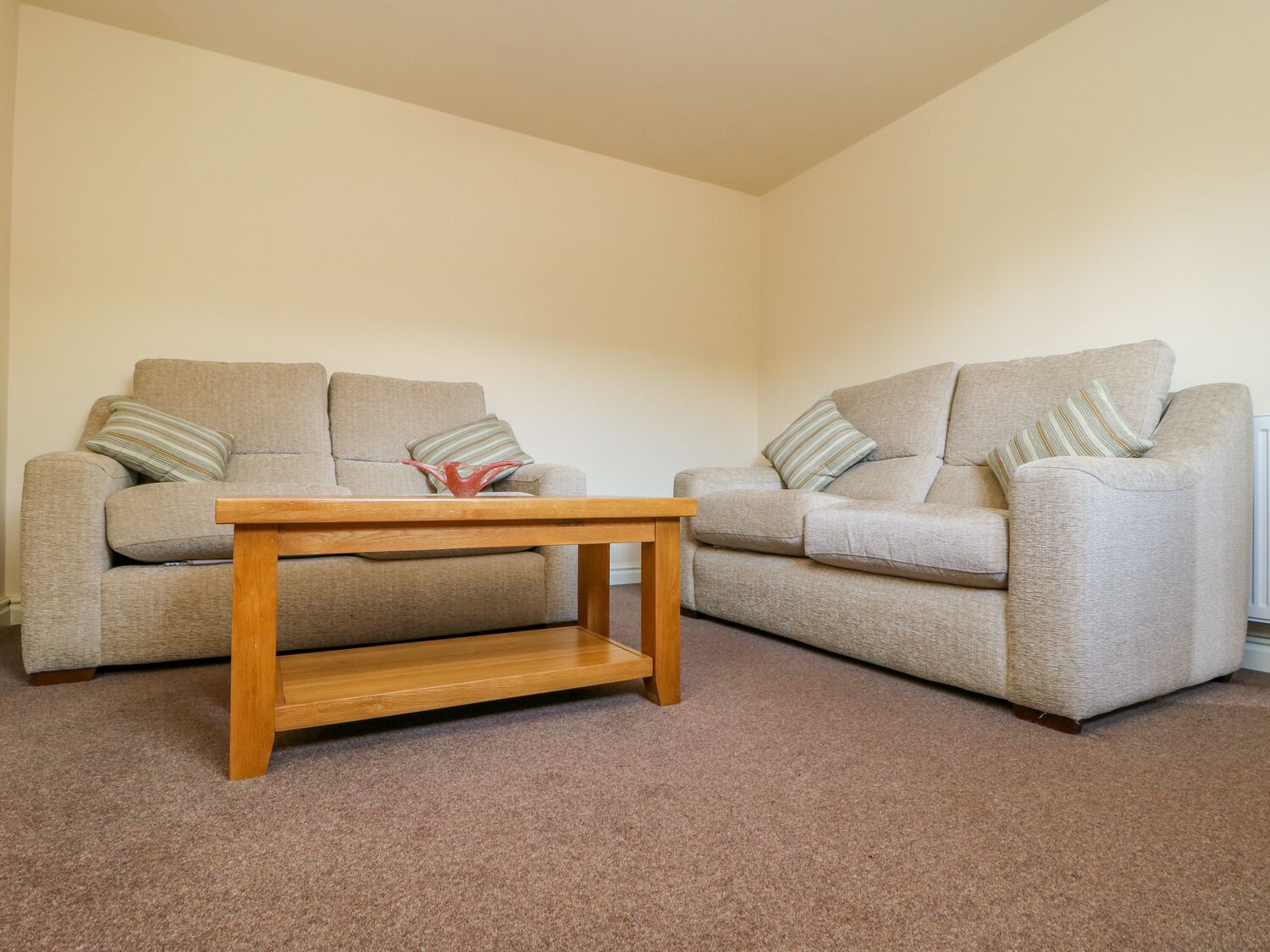 A living room with two beige sofas, a wooden coffee table, and a red decorative item on the table.