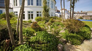 Un bâtiment blanc doté de nombreuses fenêtres et de balcons, entouré d’une végétation luxuriante et de palmiers.