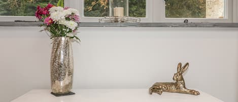 A white dresser with three drawers, a vase with flowers, a candle in a glass jar, and a golden rabbit figurine.