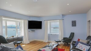 A living room with a flat-screen TV, leather sofas, a coffee table, and a view of the sea. - Gadlys House - Beau View (Beaumaris)