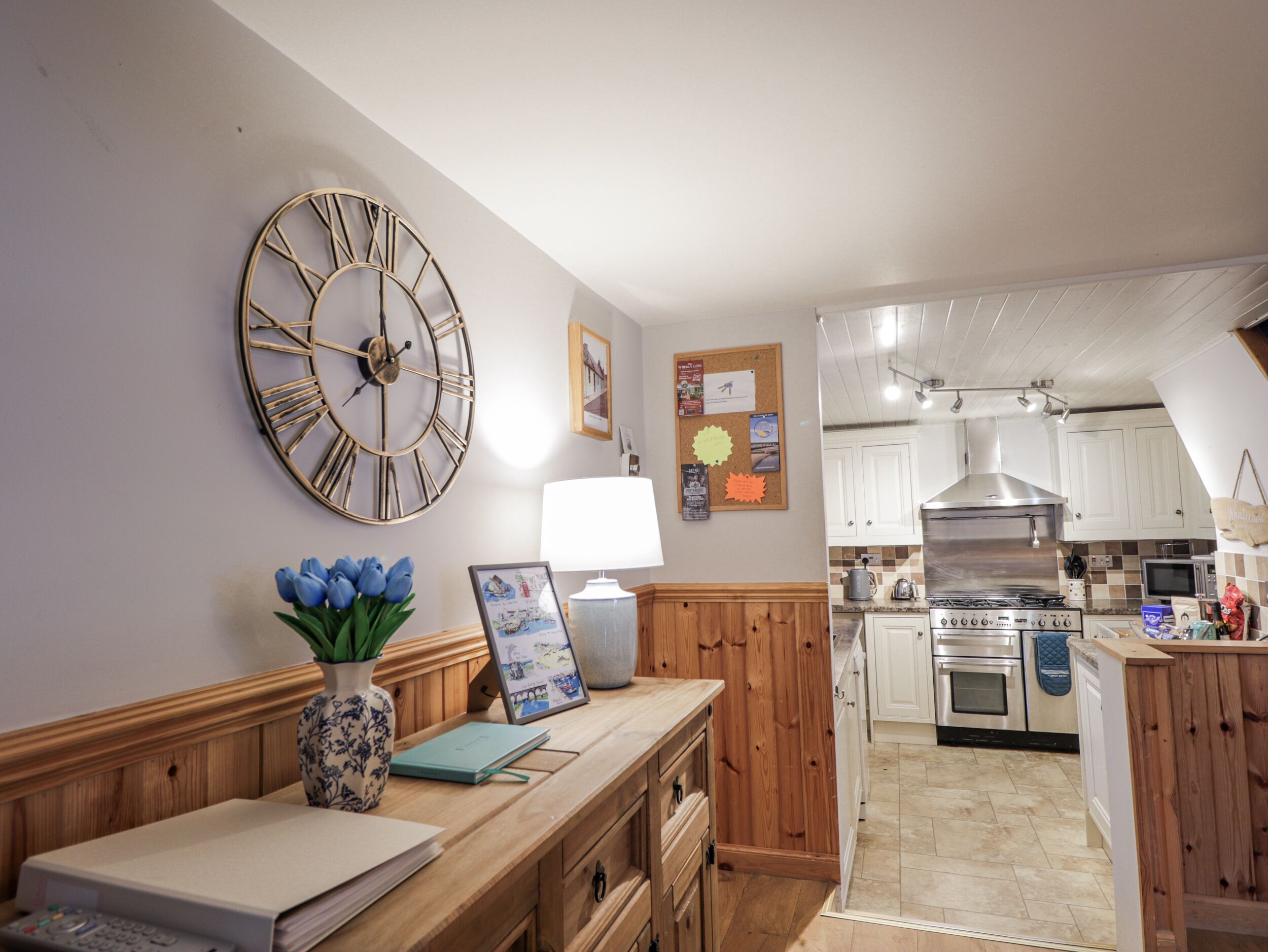 A kitchen with wooden cabinets, a stainless steel stove, and a large wall clock.