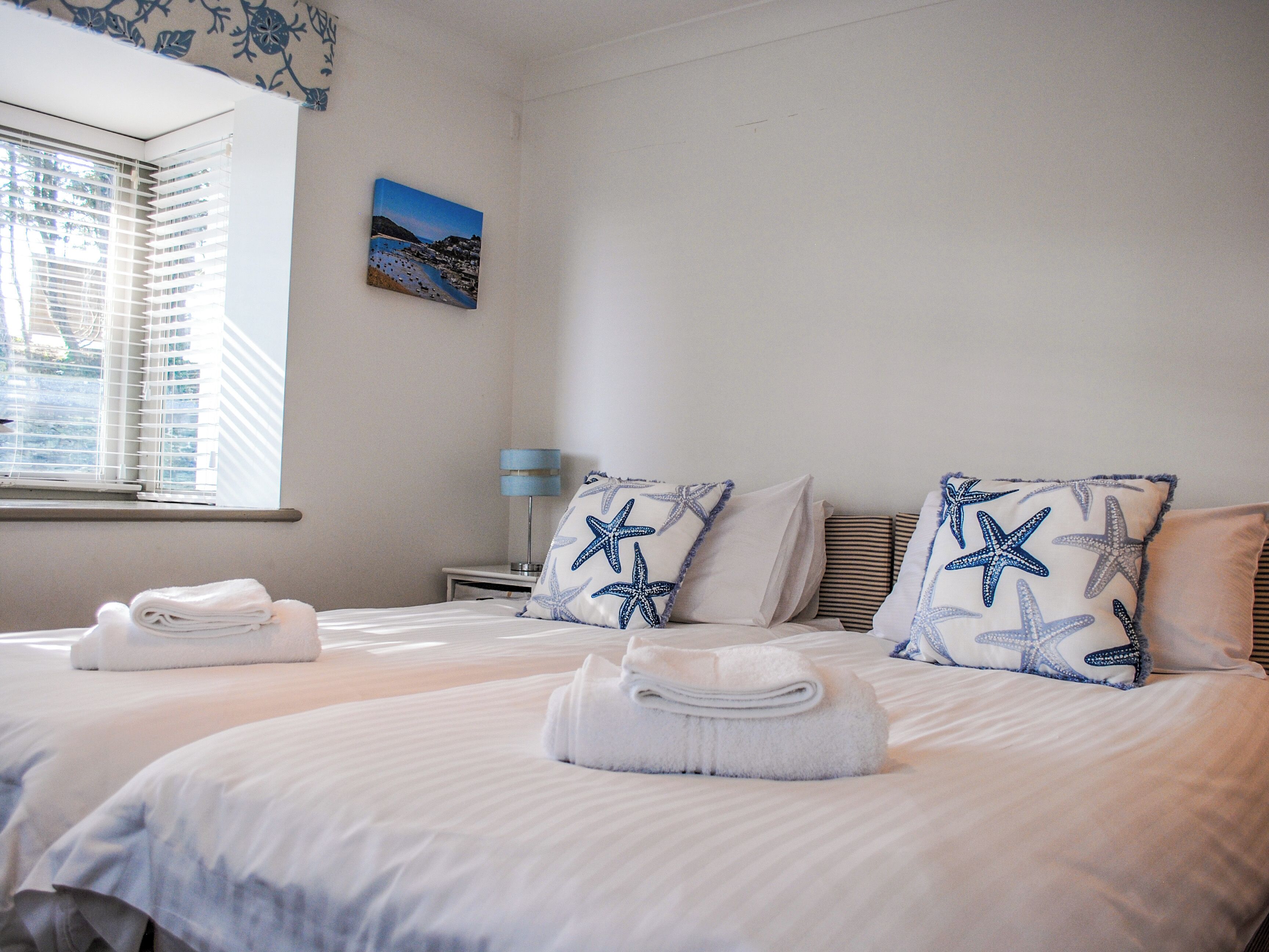 A hotel room with two beds, starfish pillows, a nightstand with a lamp, and a painting on the wall.