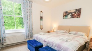 Een slaapkamer met een bed, twee nachtkastjes, een spiegel, een raam met gordijnen en een schilderij aan de muur.