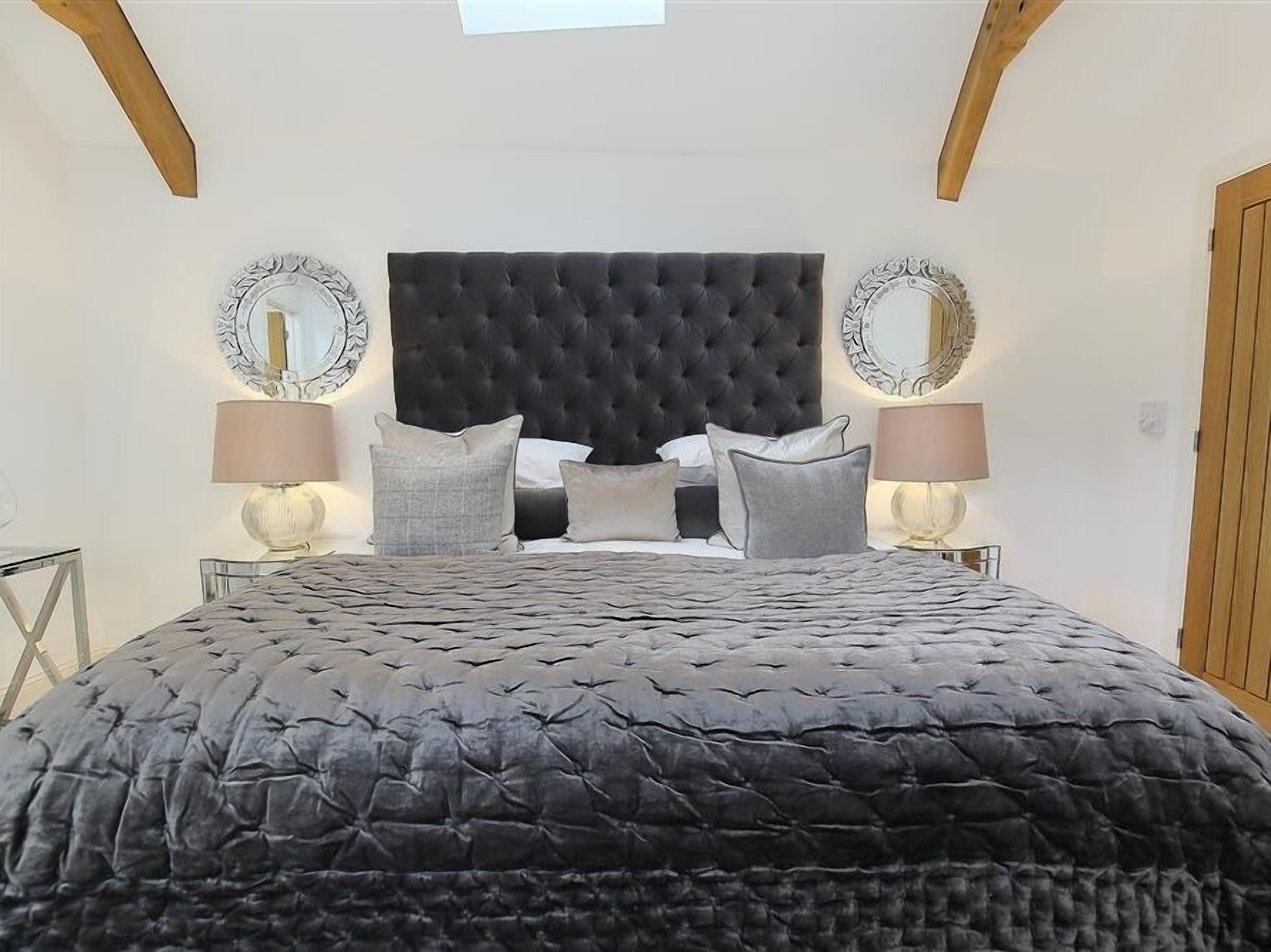 Une chambre à coucher avec une tête de lit capitonnée, deux lampes de chevet et un grand lit recouvert d’une courtepointe matelassée.