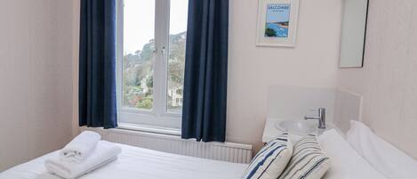 A hotel room with a bed, a window with curtains, a sink, and a framed picture on the wall.