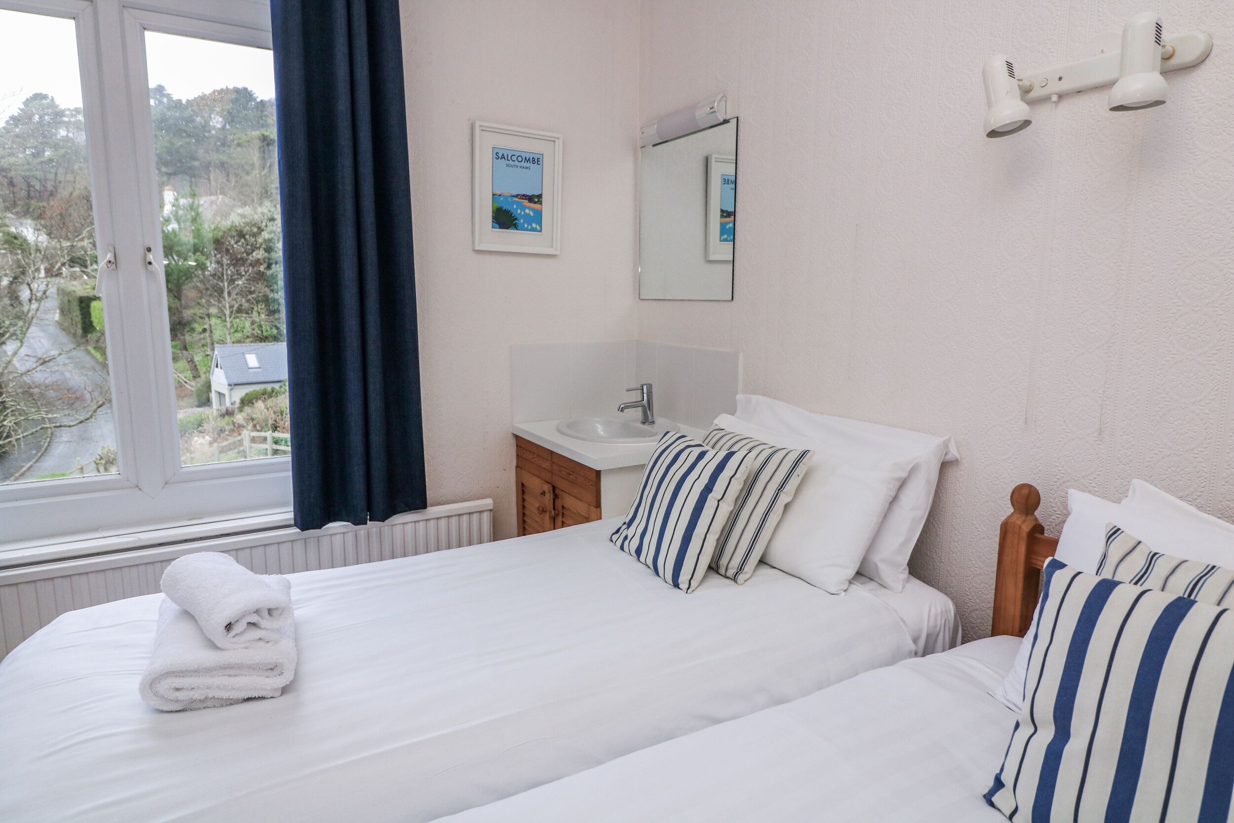 A hotel room with two beds, a window with curtains, a sink, and a mirror.