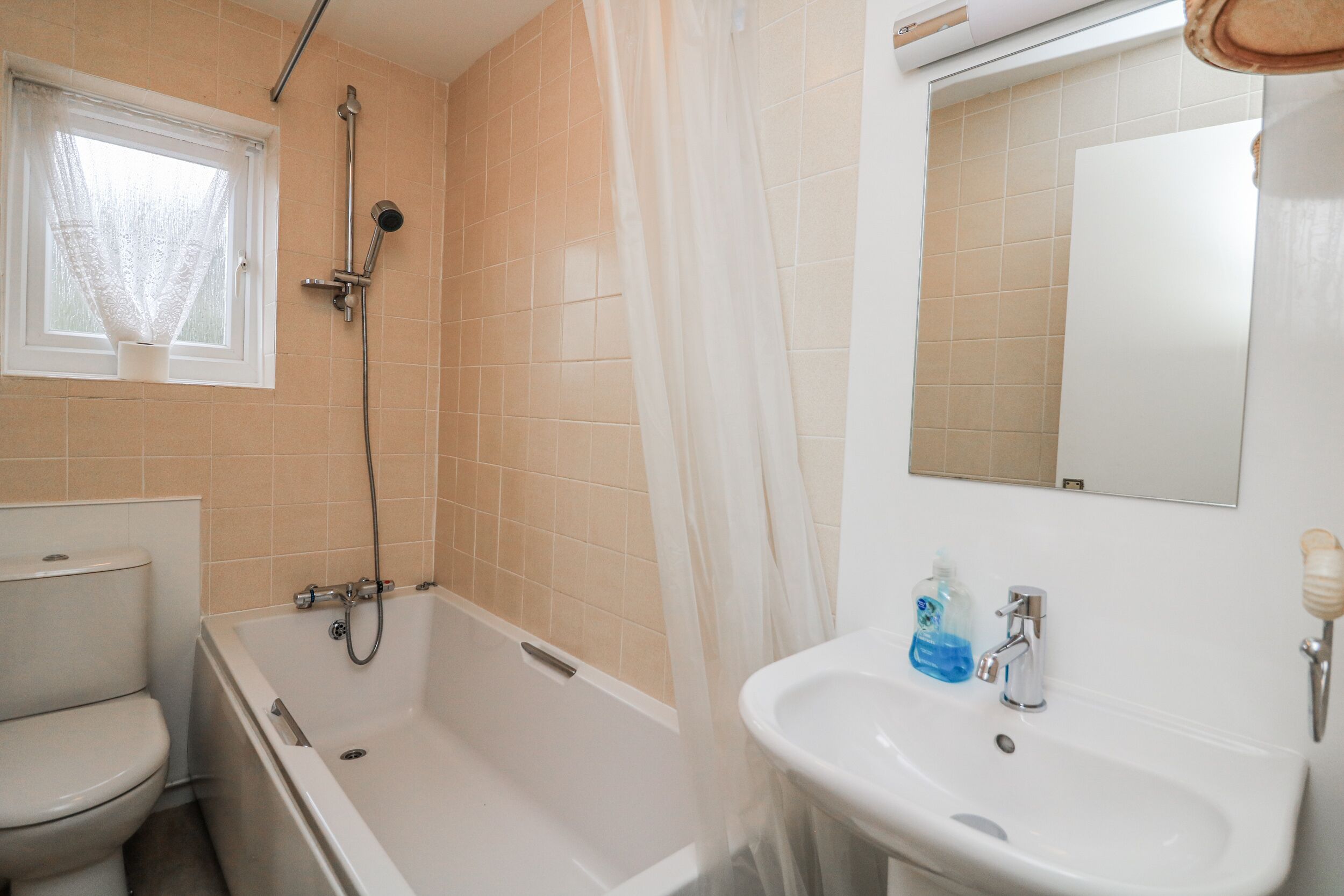 A bathroom with a bathtub, toilet, sink, and a window with a sheer curtain.