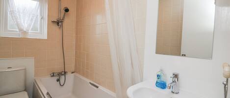 A bathroom with a bathtub, toilet, sink, and a window with a sheer curtain.