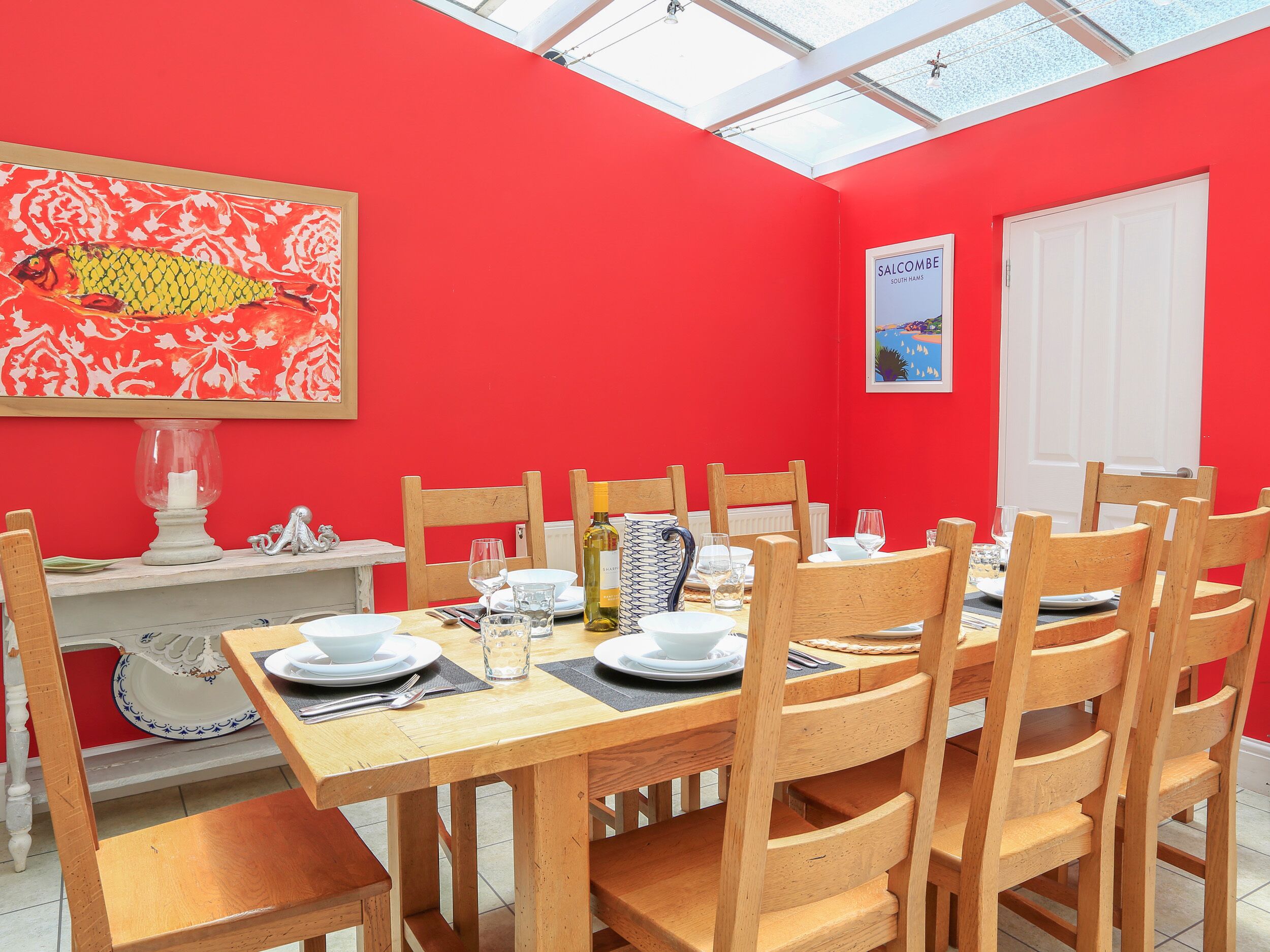 A dining area with a red wall, wooden chairs, a wooden table, and a glass ceiling.