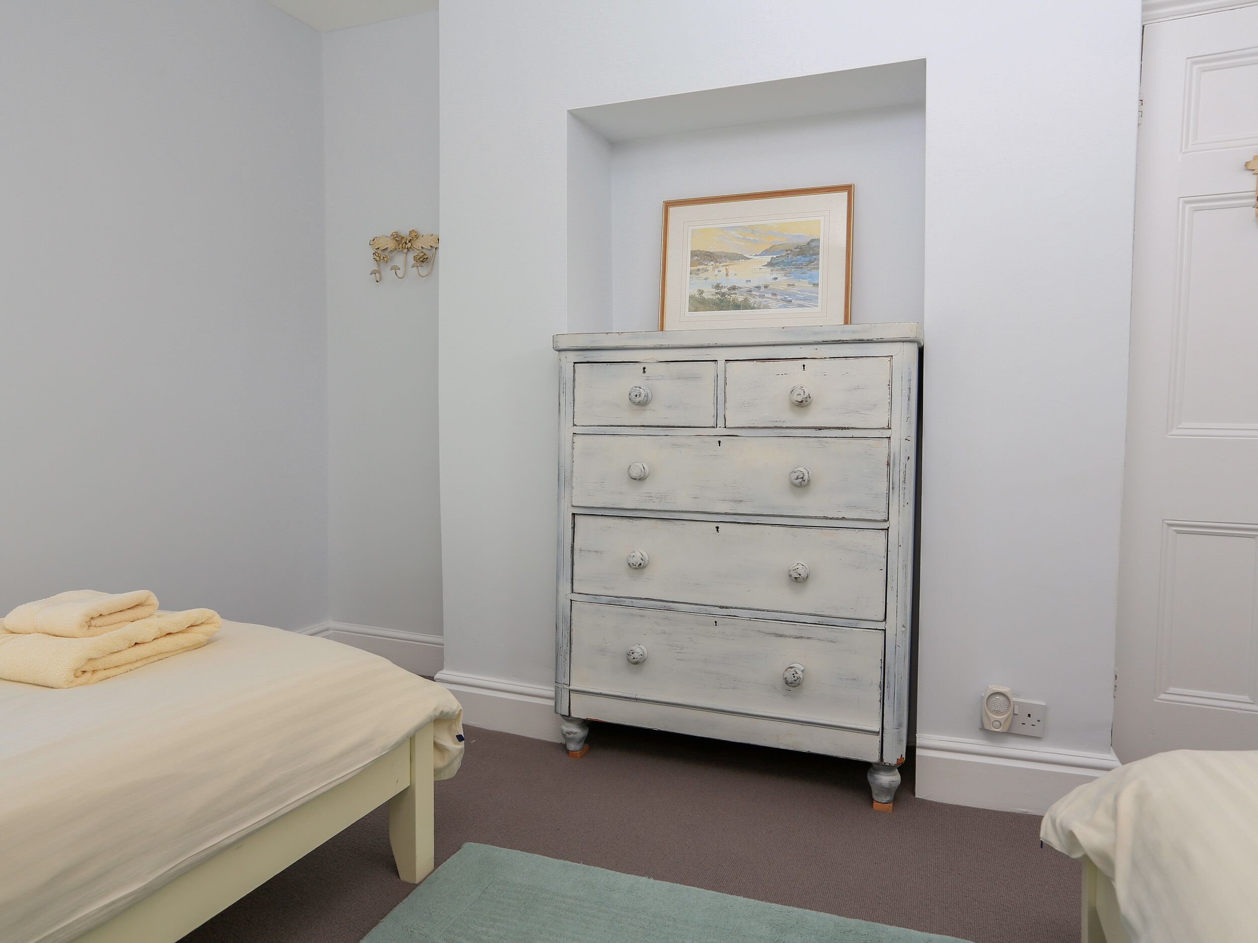 A bedroom with a bed, a dresser with drawers, a framed picture on the wall, and a small decorative item.