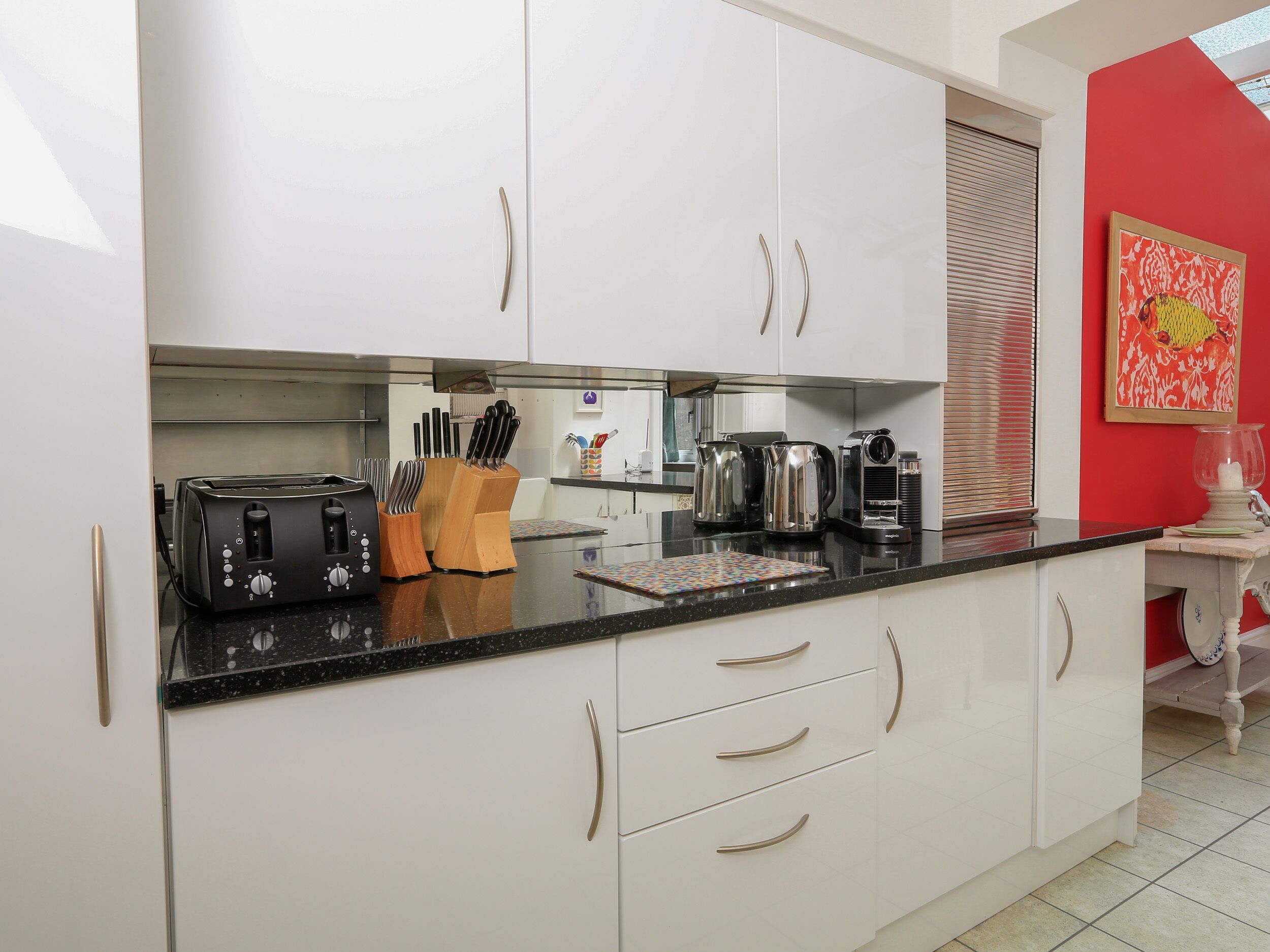 A modern kitchen with white cabinets, a black countertop, and various appliances including a toaster, coffee maker, and knife block.