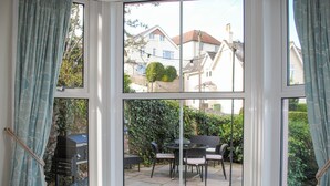 A bay window with a built-in bench, offering a view of a patio with outdoor furniture and a barbecue grill. - Wedgwood (Salcombe)