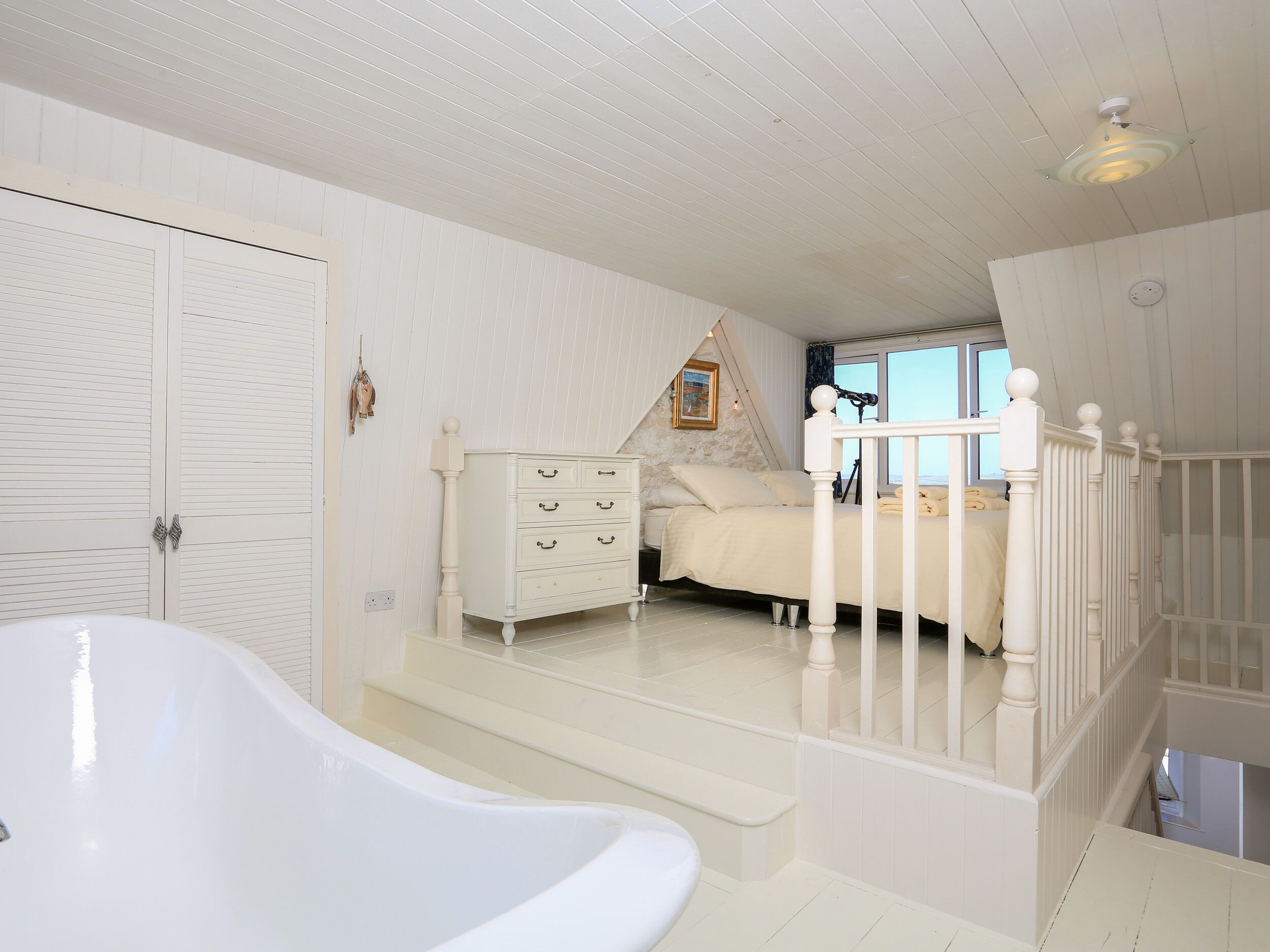 A bedroom with a bed, a dresser, a white bathtub, and a window with a view.