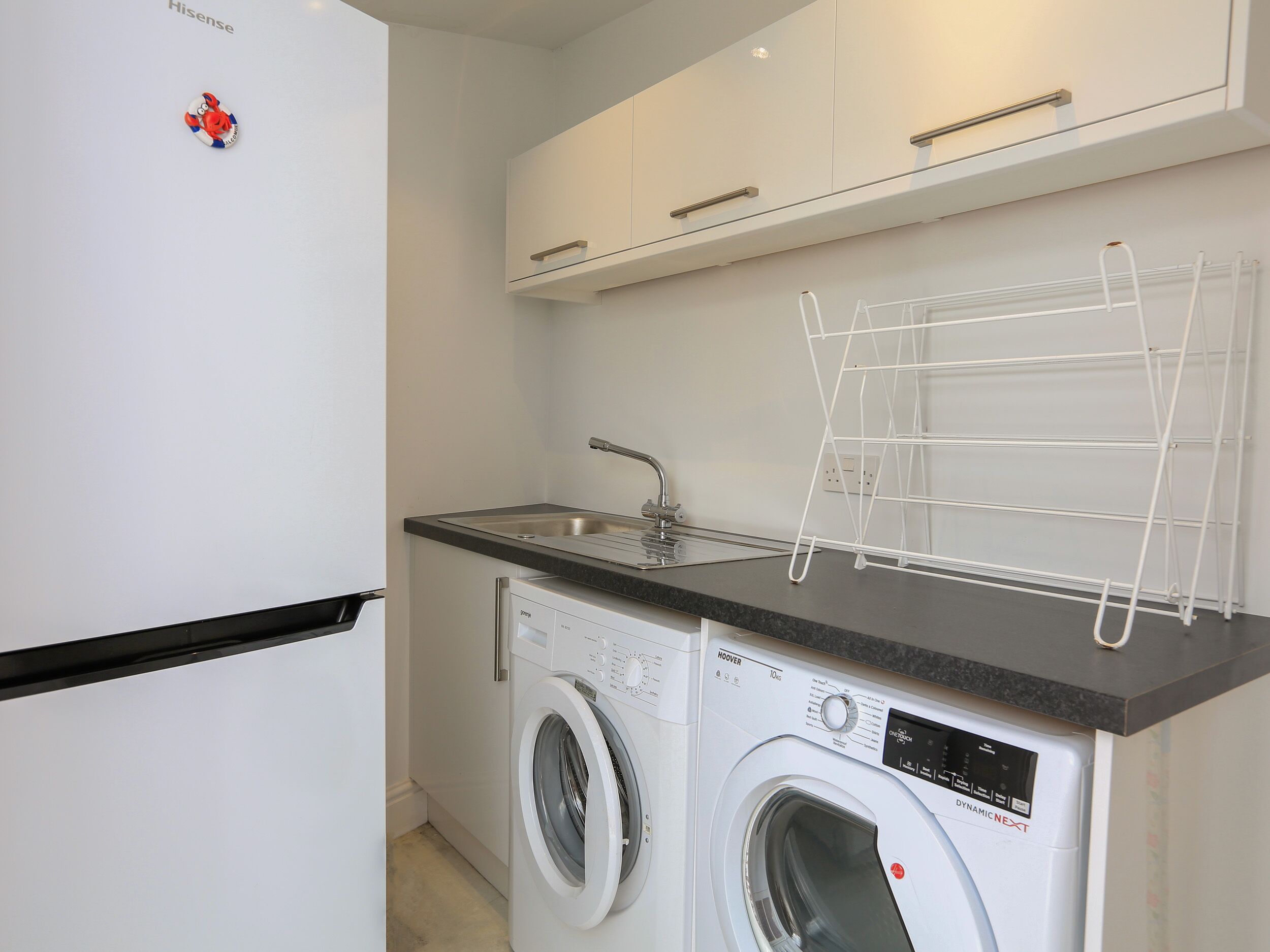 A compact kitchen with a washing machine, a sink, and a drying rack.