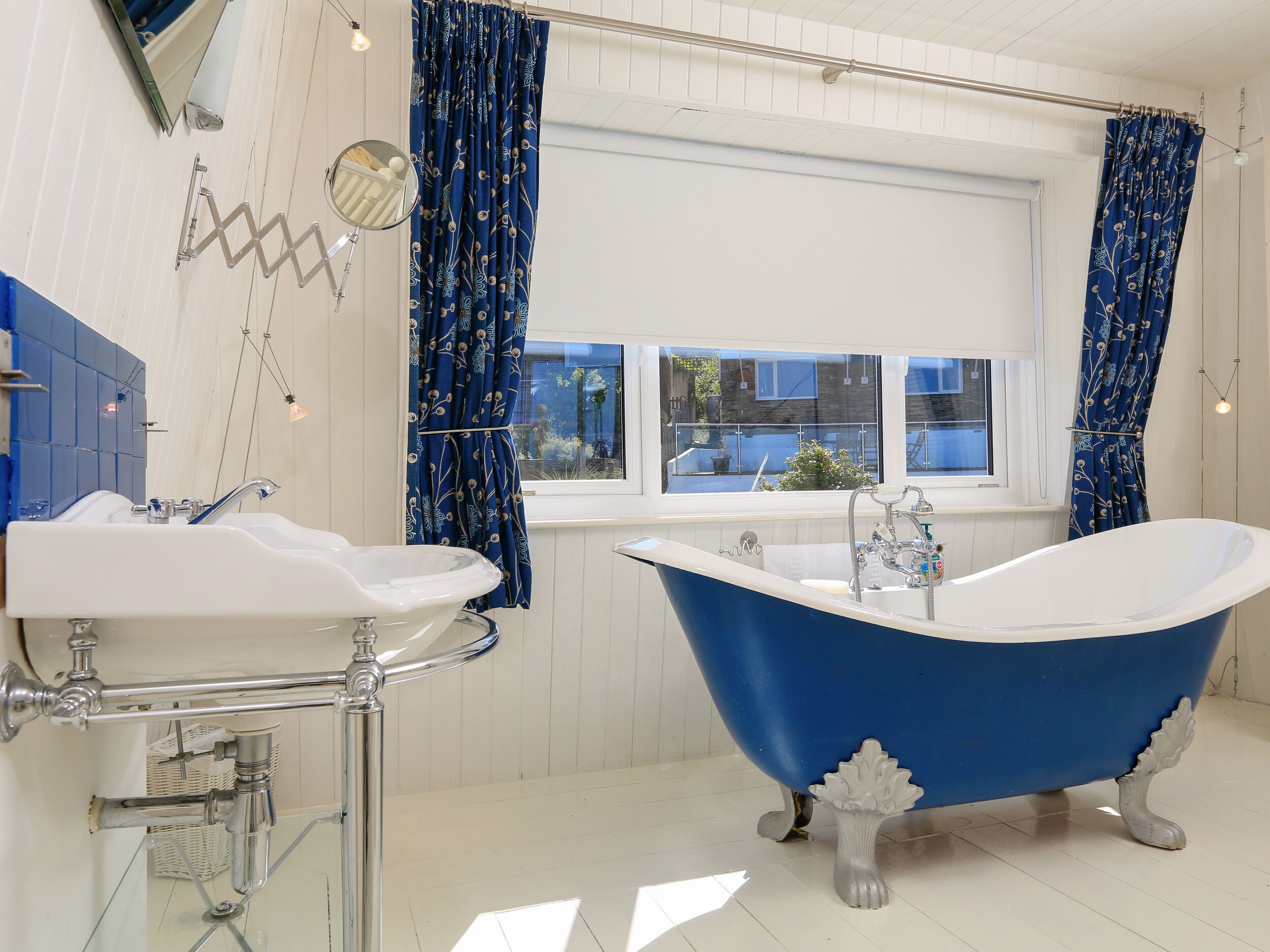Een badkamer met een witte wastafel, een blauw pootbad en een raam met uitzicht op buiten.