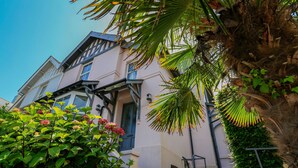 A two-story building with a balcony, stone steps, and a garden with plants and a palm tree. - Wedgwood (Salcombe)