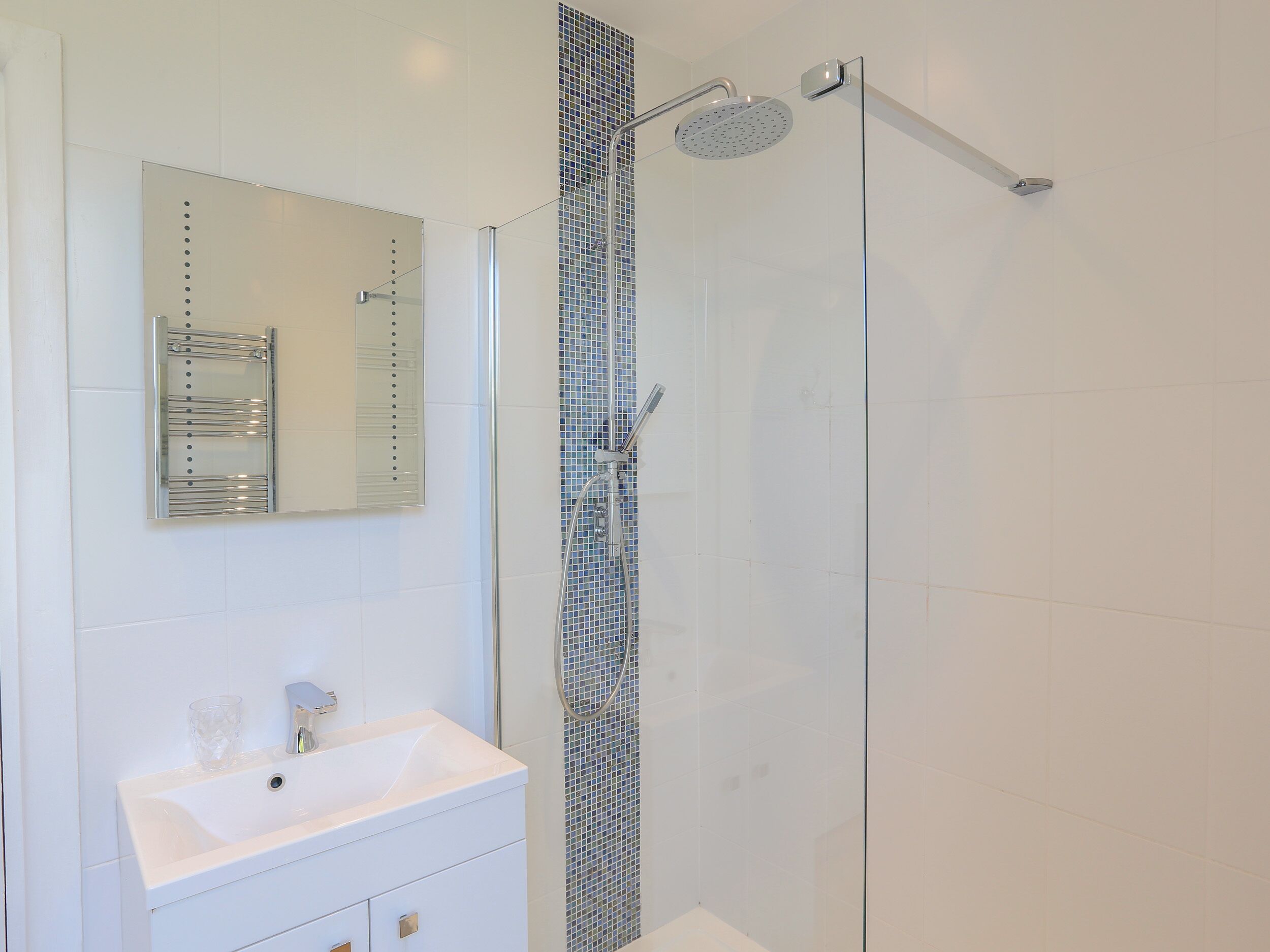Une salle de bain moderne avec une douche à parois de verre, un lavabo blanc et un miroir doté d’un porte-serviettes.