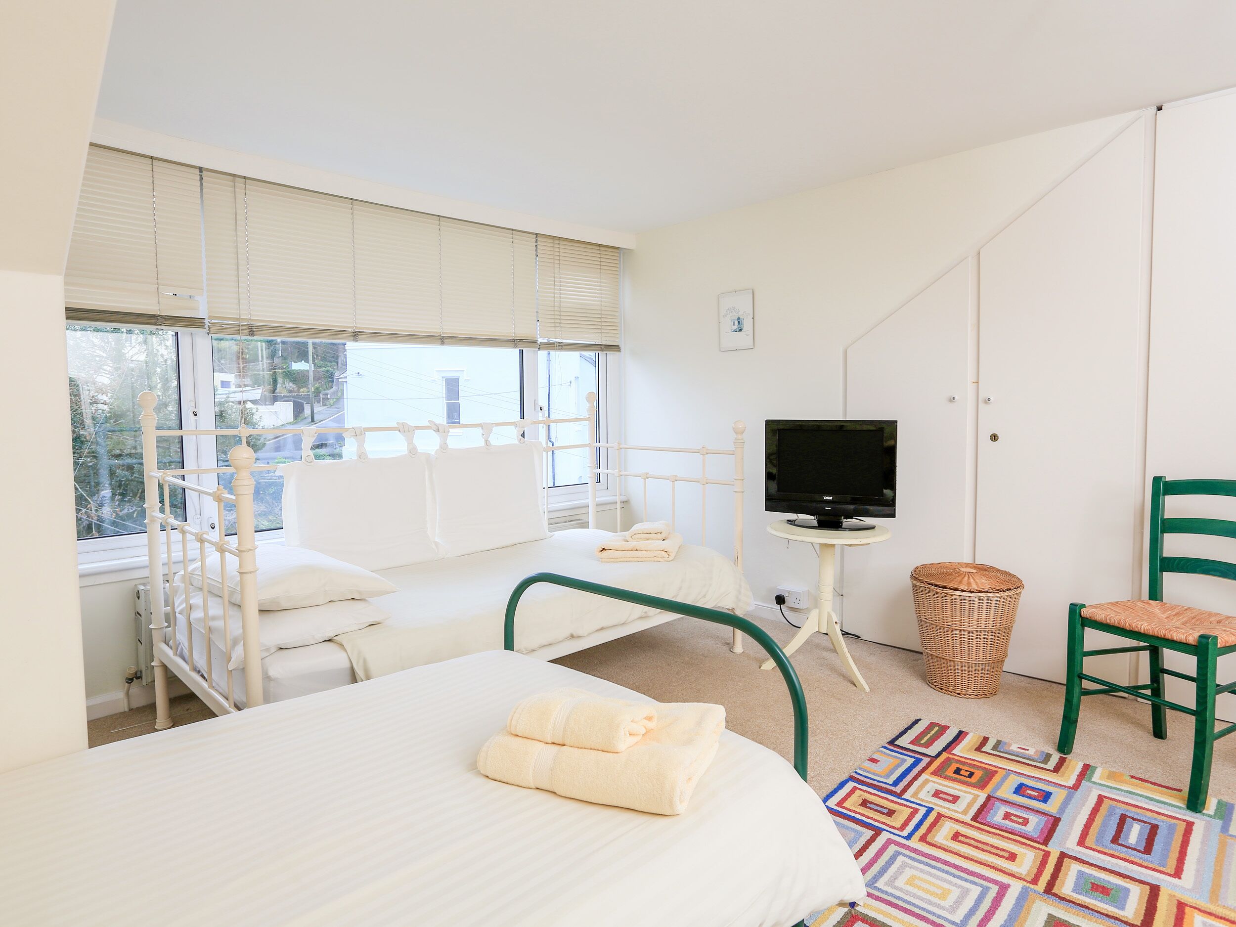A bedroom with a bed, a television on a stand, a chair, and a window with blinds.