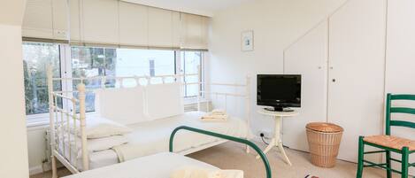 A bedroom with a bed, a television on a stand, a chair, and a window with blinds.