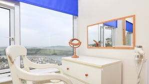 A bedroom with a view of the countryside, a white vanity with drawers, a mirror, and a hairdryer on the wall. - 2 North Crest House (Salcombe)