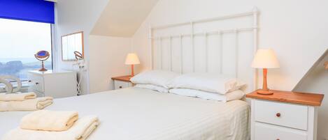 A bedroom with a bed, two bedside tables, a nightstand, a mirror, and a window with a view.