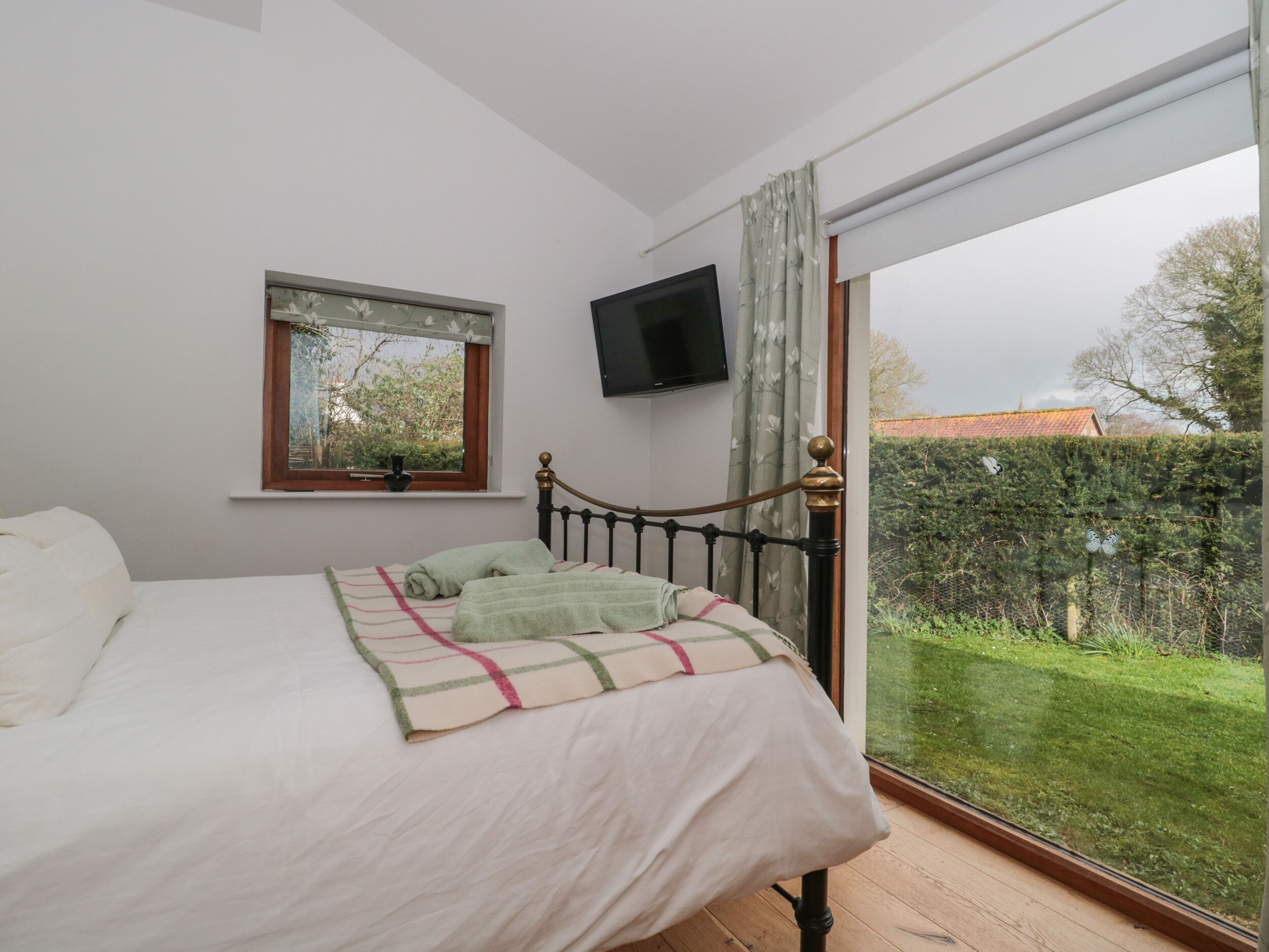 A bedroom with a bed, a window with a view of the garden, and a TV mounted on the wall.